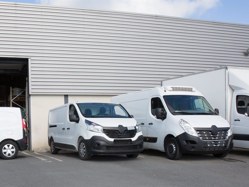 Depo önünde sıralanmış beyaz kapalı kasa minivan filosu